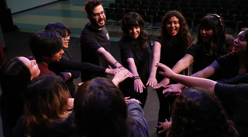 A photograph of a group of twelve people including students and instructors putting their hands in for a cheer. Everyone is smiling.