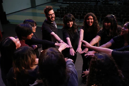 A photograph of a group of twelve people including students and instructors putting their hands in for a cheer. Everyone is smiling.