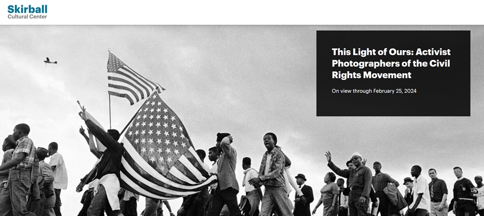 The image shows a group of people holding a flag at the Skirball Cultural Center. The exhibition "This Light of Ours: Activist Photographers of the Civil Rights Movement" is on view at the center through February 25, 2024. The photo features text, clothing, a man, a poster, the flag, the sky, people, and an outdoor presentation.