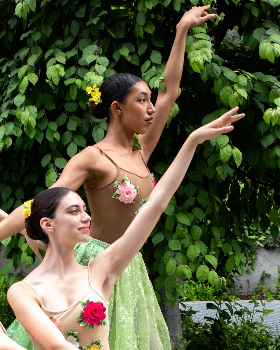 The image shows two women wearing white dresses. One of the women is dancing. The background includes flowers.